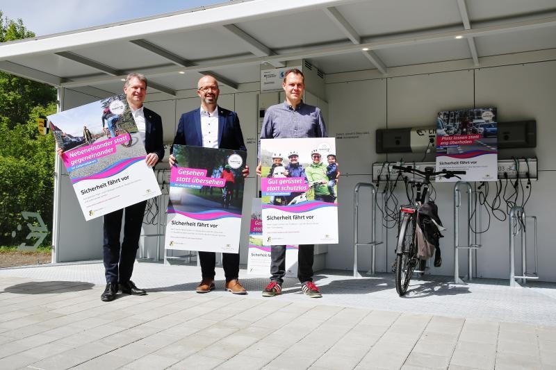 Drei Männer halten Plakate zum Thema Radfahrsicherheit in den Händen. 