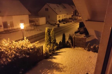Schnee fällt, ein Garten und eine Straße sind weiß