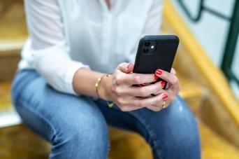 Frau sitzt auf einer Steintreppe mit einem Handy in der Hand 