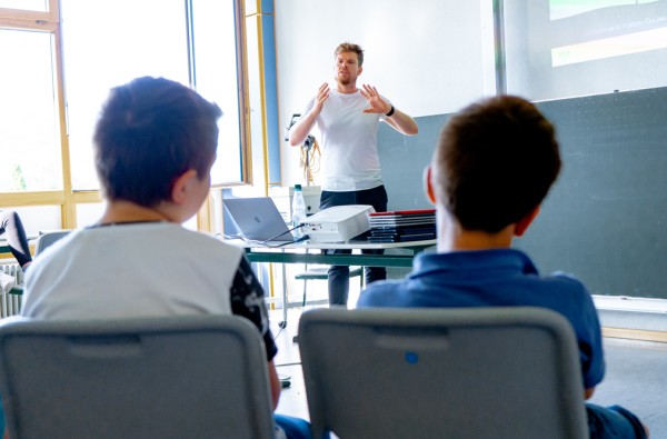 Ein Mann steht vorne an der Tafel in einem Klassenzimmer und hält einen Vortrag. 