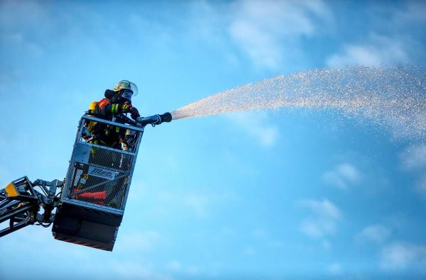 Ein Feuerwehrmann spritzt vom Drehleiterkorb aus Wasser aus einem Schlauch