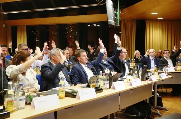 Breite Zustimmung geben die Kreistagsmitglieder dem Haushalt für 2025. ©Landratsamt Zollernalbkreis Männer und Frauen in einem Saal an Tischen, sie signalisieren Zustimmung durch erhobene Hände