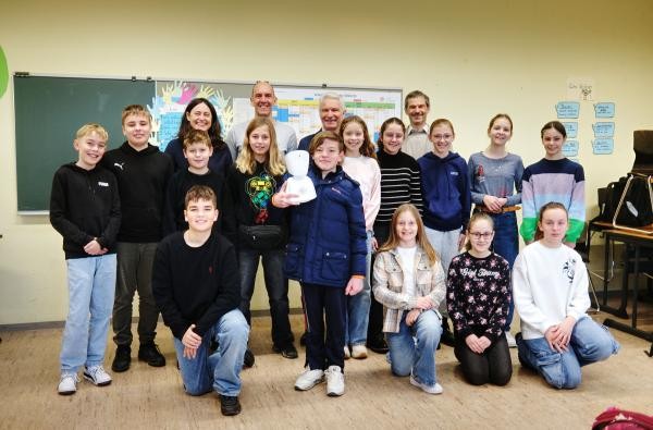 Jonas hält den AV1-Avatar - über den Roboter hielt er während seiner Erkrankung Kontakt zu seiner Klasse am Progymnasium Rosenfeld. Karl Wolf, Dezernent der Hauptverwaltung im Landratsamt, sowie Christoph Abt, Leiter des Kreismedienzentrums, überzeugten sich bei einem Besuch an der Schule von den Fähigkeiten des AV1. ©Landratsamt Zollernalbkreis Mehrere Jugendliche stehen mit Erwachsenen in einem Klassenzimmer