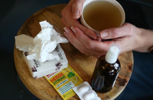 Tee, Taschentücher, Medikamente gehören zum Standardprogramm bei einer Grippeerkrankung. ©Landratsamt Zollernalbkreis Eine Frau hält eine Tasse Tee, vor ihr liegen auf dem Tisch Medikamente und Taschentücher