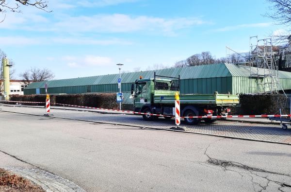 Die Parkplätze vor der Kreissporthalle Hechingen sind abgesperrt. Die Arbeiten für die grundlegende Sanierung des Hallendachs haben begonnen. ©Landratsamt Zollernalbkreis Eine Straße mit Parkplätzen diese sind abgesperrt. Dahinter die Kreissporthalle Hechingen