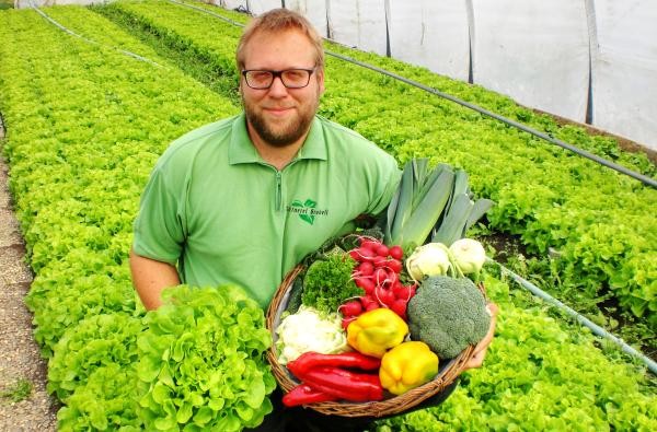 In der Gärtnerei von Jörg Brobeil in Geislingen erhalten Interessierte spannende Informationen zu Anbau und Vermarktung von regionalem Gemüse und Obst. ©Landratsamt Zollernalbkreis Ein Mann - Jörg Brobeil - steht in einem Gewächshaus voller Salate und hält Gemüse in der Hand.