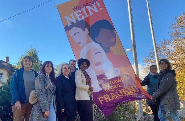 Beim Hissen der Fahne: Landrat Günther-Martin Pauli, Estelle Koschnike-Nguewo (Vierte von links) sowie Vertreterinnen des Frauenhauses, des Vereins Feuervogel, des Weißen Rings, der Selbsthilfegruppe Häusliche Gewalt und des Frauennetzwerks Zollernalb. ©Landratsamt Zollernalbkreis Ein Mann - Landrat Pauli - und mehrere Frauen halten eine Fahne. Darauf ist zu lesen: Wir sagen Nein zu Gewalt gegen Frauen.