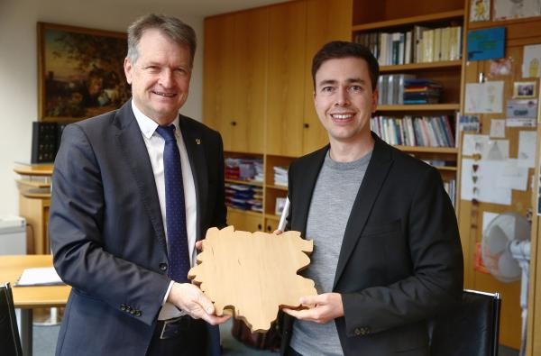 Herzlich willkommen im Zollernalbkreis: Landrat Günther-Martin Pauli (links) überreicht Sigurd Quast zum Start ein Vesperbrett in Form der Landkreissilhouette. ©Landratsamt Zollernalbkreis Zwei Männer in einem Büro - Landrat Günther-Martin Pauli und Sigurd Quast.