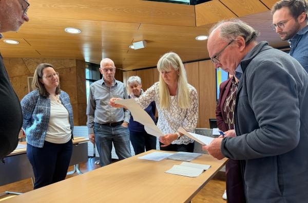 Kreiswahlleiterin Petra Hahn (Mitte) prüft mit den Mitgliedern des Kreiswahlausschusses einzelne Stimmzettel. Das Gremium hat am Freitag das endgültige Ergebnis der Landtagswahl im Wahlkreis 63 Balingen festgestellt. ©Landratsamt Zollernalbkreis Mehrere Personen stehen um einen Tisch und schauen Wahlzettel an.