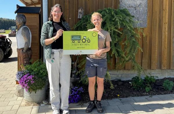 Carolin Dietz vom Landwirtschaftsamt (links) und Katrin Brobeil von der Bio Agrar GbR © Landratsamt Zollernalbkreis zwei Frauen mit einem Schild zum Lernort Bauernhof