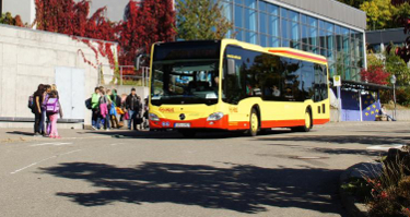 Schülerinnen und Schüler an einer Bushaltestelle mit Bus