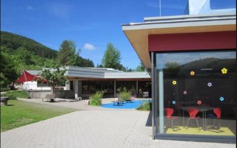 Außenansicht Rossentalschule Albstadt mit Blick in ein verglastes Klassenzimmer bei schönem Wetter mit Blick auf den Pausenhof und die Grünanlage 