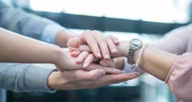 Hände von fünf Persoenen übereinandergelegt